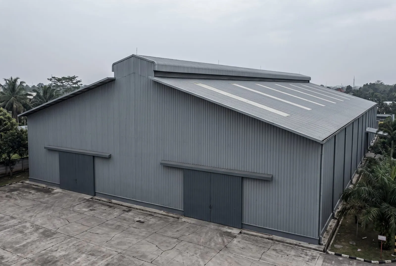 Tampak luar bangunan produksi dengan dinding metal tinggi dan ventilasi bubungan sepanjang atap.